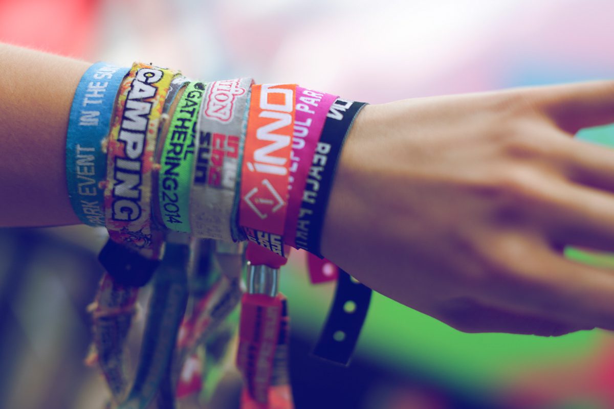 Close-up of a person’s wrist covered in colourful fabric event wristbands, representing past music festivals and Innovation Events experiences.